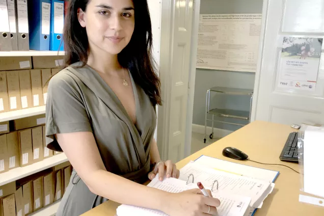 Sara Maroufkhani på sitt kontor. Bakom sig har hon ett skåp med pärmar och framför sig en pärm med blanketter. Foto.