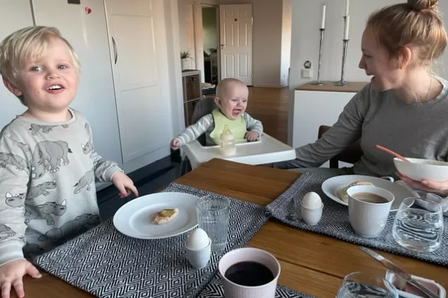 Två barn och deras mamma vid frukostbordet. De tittar på varandra och ser glada ut. Foto.