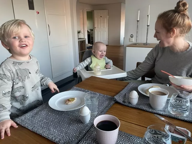 Två barn och deras mamma vid frukostbordet. De tittar på varandra och ser glada ut. Foto.